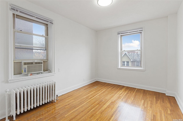 spare room with radiator heating unit, cooling unit, a textured ceiling, and hardwood / wood-style flooring