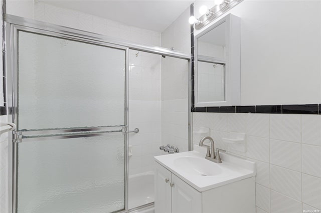 bathroom with combined bath / shower with glass door, vanity, and tile walls