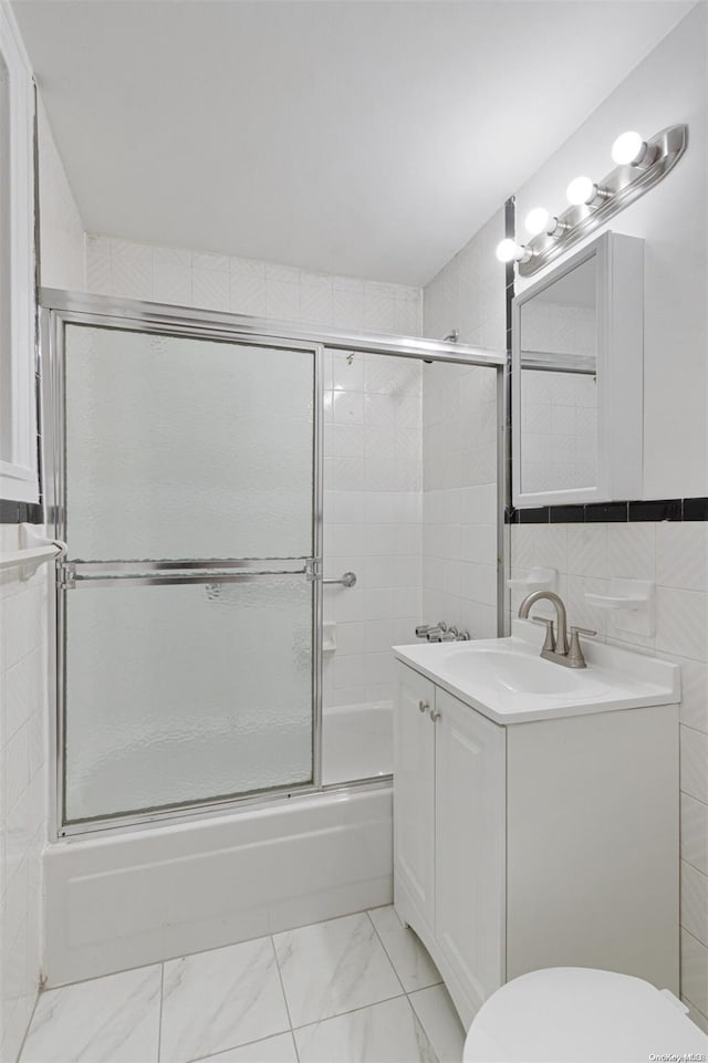 full bathroom with combined bath / shower with glass door, vanity, toilet, and tile walls