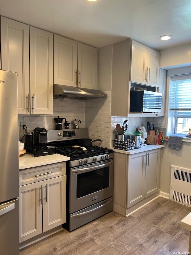 kitchen featuring radiator heating unit, tasteful backsplash, light hardwood / wood-style floors, white cabinets, and appliances with stainless steel finishes