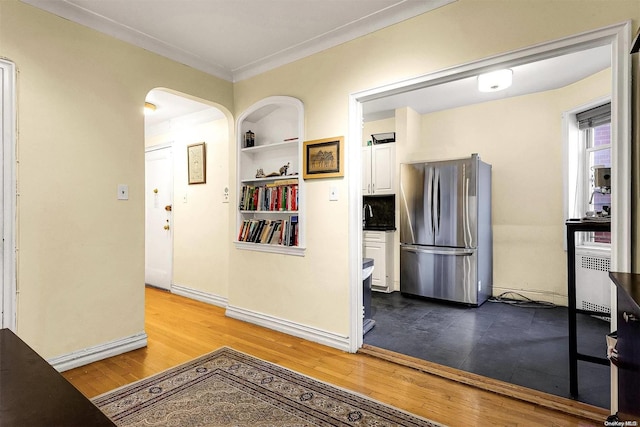 kitchen with built in shelves, crown molding, hardwood / wood-style flooring, white cabinets, and stainless steel refrigerator