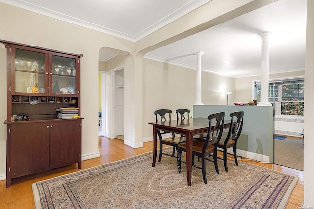 dining space featuring light wood-type flooring, crown molding, and ornate columns