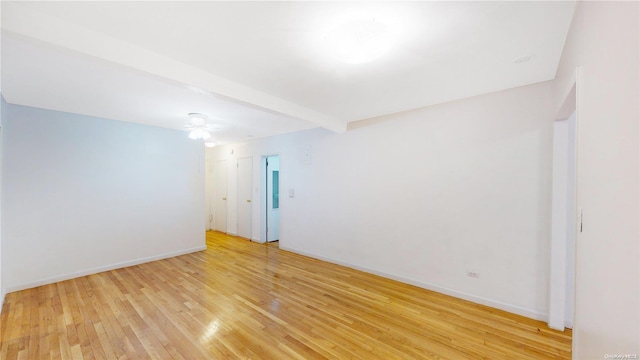 unfurnished room with beamed ceiling and light wood-type flooring