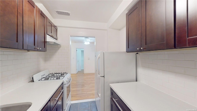 kitchen with white appliances, ceiling fan, backsplash, dark brown cabinets, and range hood