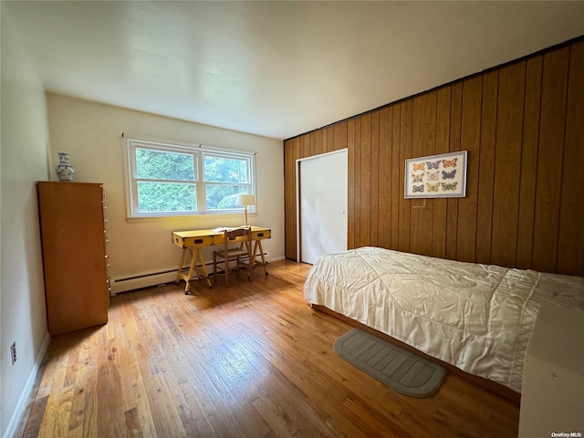 bedroom with wood walls, a baseboard heating unit, and light wood-type flooring