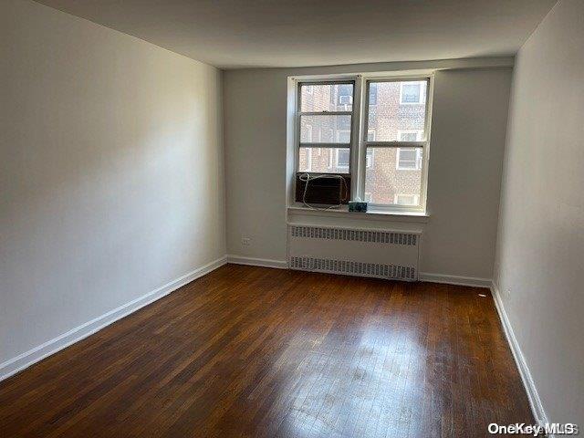 spare room with radiator heating unit, cooling unit, and dark wood-type flooring