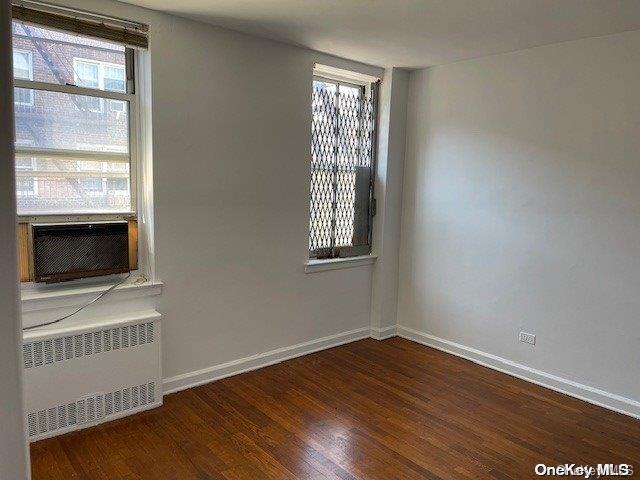 spare room with radiator heating unit, dark hardwood / wood-style flooring, and cooling unit