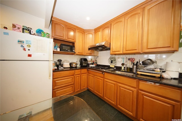 kitchen with gas cooktop, tasteful backsplash, sink, white refrigerator, and dark stone countertops