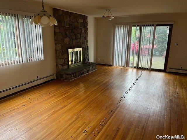 unfurnished living room featuring hardwood / wood-style flooring, a healthy amount of sunlight, a stone fireplace, and a baseboard radiator