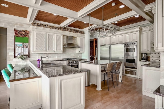 kitchen with a breakfast bar, a center island, wall chimney exhaust hood, appliances with stainless steel finishes, and kitchen peninsula