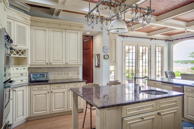 kitchen with a kitchen island with sink, french doors, sink, light hardwood / wood-style flooring, and cream cabinetry