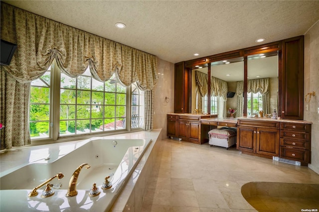 bathroom with a textured ceiling, vanity, and tiled tub