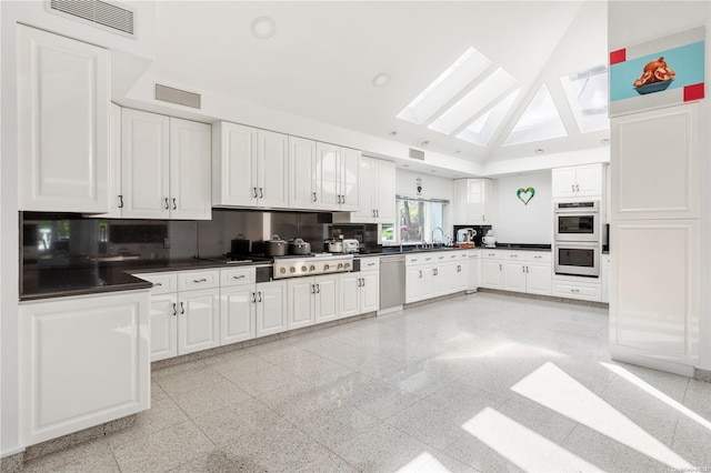 kitchen featuring tasteful backsplash, white cabinetry, lofted ceiling with skylight, and appliances with stainless steel finishes