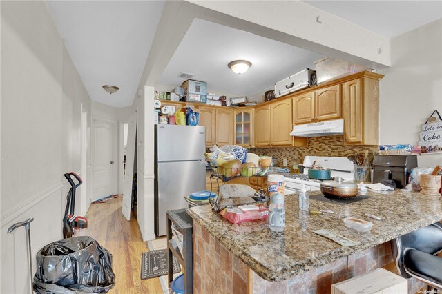 kitchen featuring a kitchen breakfast bar, light wood-type flooring, light stone counters, white stove, and stainless steel refrigerator