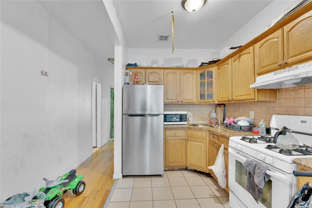 kitchen featuring light stone countertops, sink, light hardwood / wood-style flooring, backsplash, and white appliances