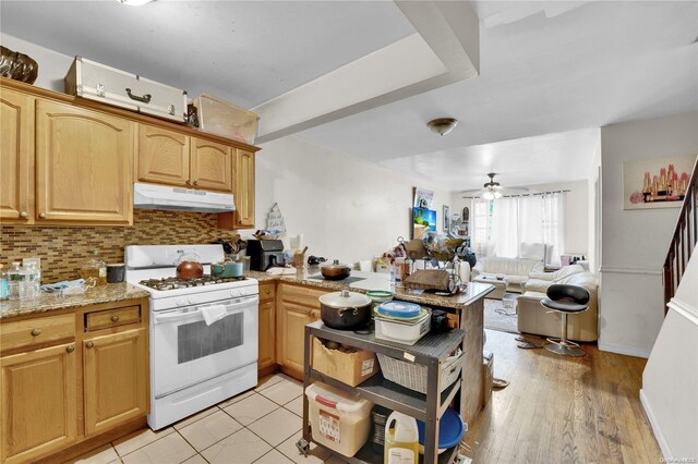 kitchen featuring light stone countertops, kitchen peninsula, light wood-type flooring, white gas range, and ceiling fan