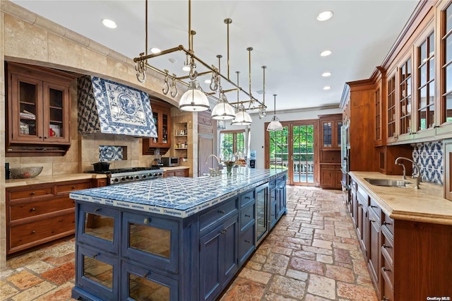 kitchen with decorative backsplash, premium range hood, sink, hanging light fixtures, and a large island