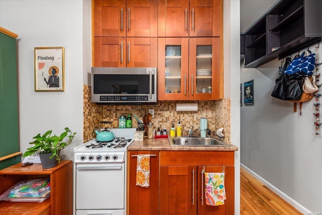 kitchen with sink, white stove, light hardwood / wood-style flooring, and backsplash