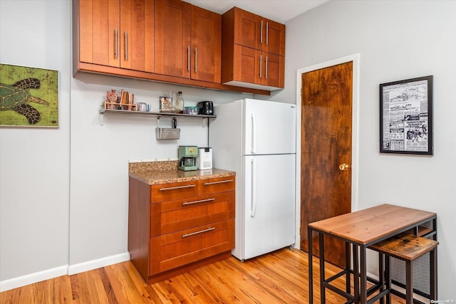 kitchen with light stone countertops, light hardwood / wood-style floors, and white refrigerator