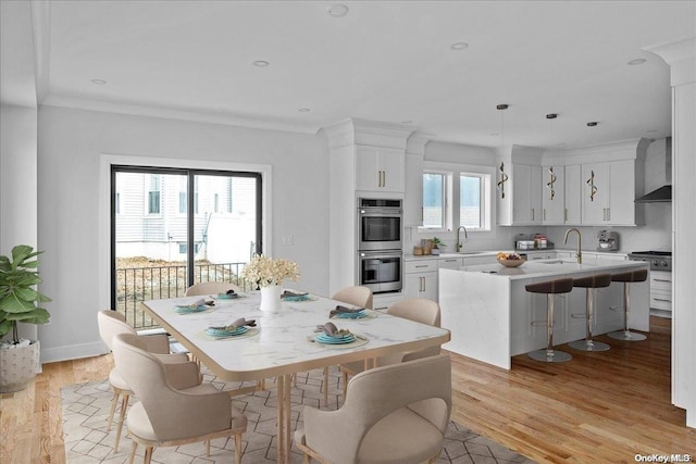 dining space featuring light wood-type flooring, a wealth of natural light, crown molding, and sink