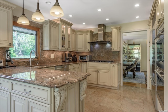 kitchen featuring pendant lighting, wall chimney range hood, cream cabinets, and dark stone counters