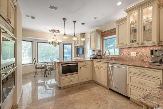 kitchen with sink, hanging light fixtures, light stone counters, stainless steel appliances, and cream cabinetry