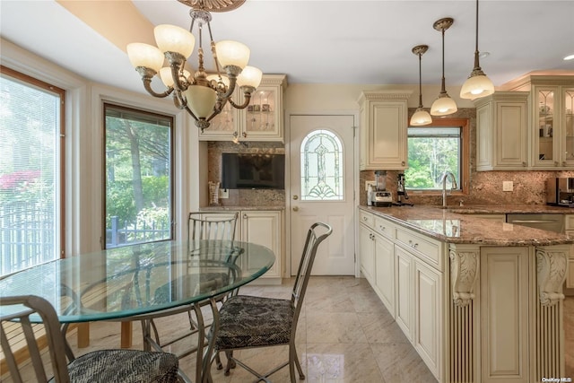 kitchen with sink, light stone counters, tasteful backsplash, decorative light fixtures, and cream cabinetry