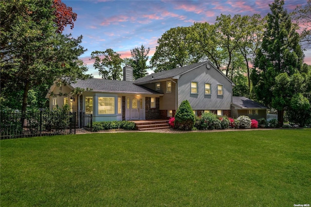 split level home featuring fence, covered porch, stone siding, a front yard, and a chimney