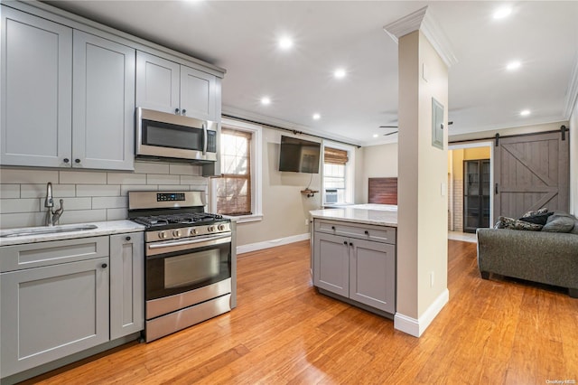 kitchen featuring gray cabinetry, crown molding, sink, a barn door, and stainless steel appliances