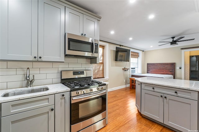 kitchen featuring sink, light hardwood / wood-style flooring, gray cabinets, decorative backsplash, and appliances with stainless steel finishes