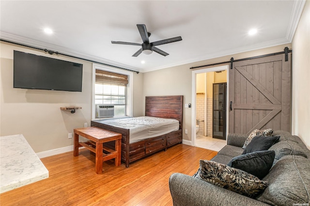 bedroom with a barn door, ceiling fan, ensuite bath, and light wood-type flooring