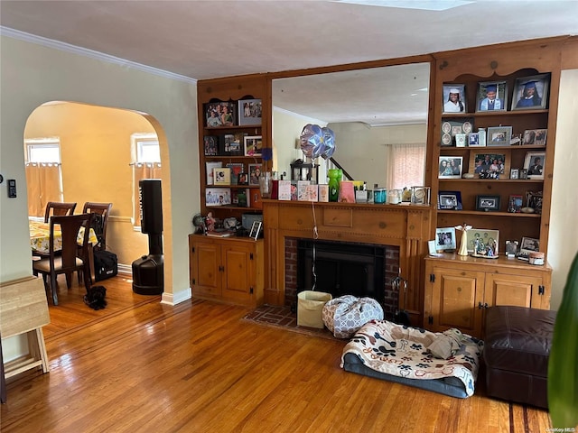 living room featuring hardwood / wood-style flooring, crown molding, and a brick fireplace