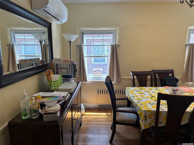 dining room with a wall unit AC, radiator, a wealth of natural light, and wood-type flooring