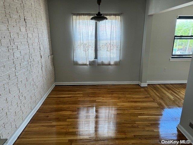 unfurnished dining area featuring dark wood-type flooring and brick wall