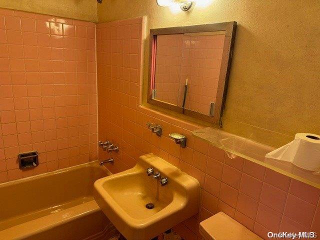 bathroom with tile walls, sink, and tiled shower / bath