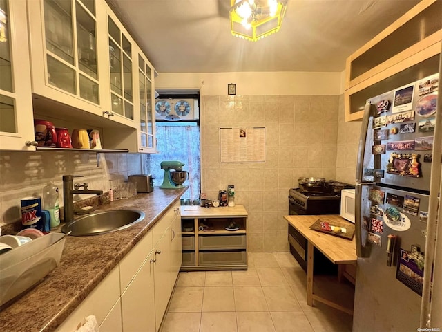 kitchen featuring stainless steel fridge, light stone counters, sink, light tile patterned floors, and white cabinets