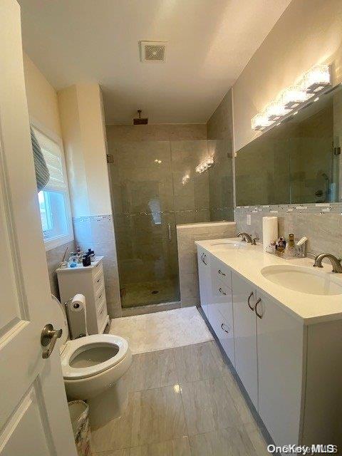 bathroom with tasteful backsplash, vanity, a shower with door, tile walls, and toilet