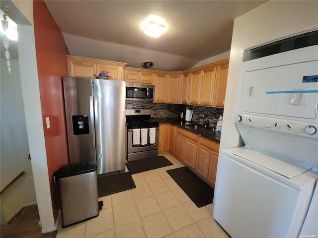 kitchen featuring sink, stacked washer and dryer, light tile patterned floors, appliances with stainless steel finishes, and tasteful backsplash