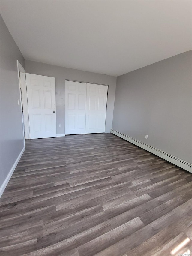 unfurnished bedroom with dark hardwood / wood-style flooring, baseboard heating, and a closet