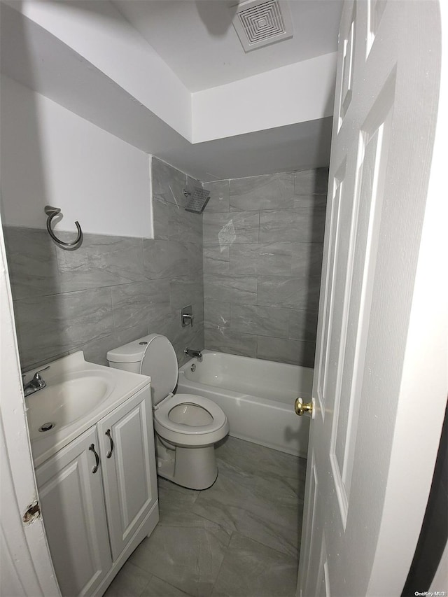 full bathroom with tiled shower / bath combo, toilet, tile walls, and vanity