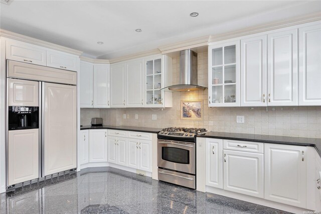 kitchen featuring white cabinets, paneled built in fridge, wall chimney range hood, gas range, and tasteful backsplash