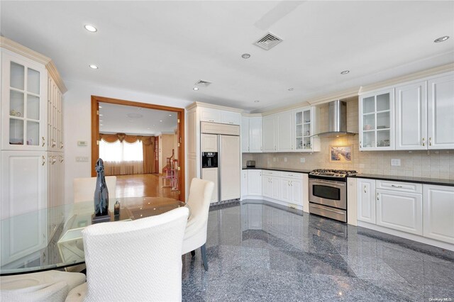 kitchen with white cabinets, wall chimney exhaust hood, decorative backsplash, paneled fridge, and stainless steel range with gas stovetop