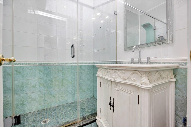 bathroom with a shower with door, vanity, and tile walls