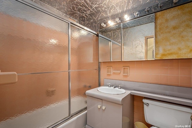 full bathroom featuring toilet, vanity, tile walls, and combined bath / shower with glass door