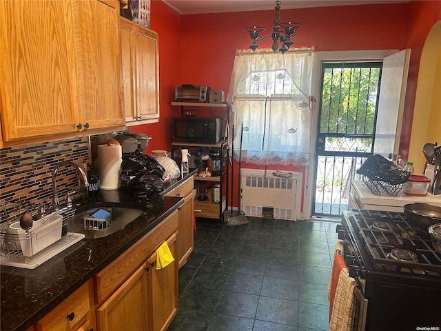 kitchen featuring decorative backsplash, dark stone counters, black appliances, pendant lighting, and radiator heating unit