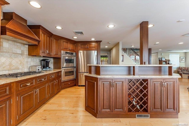 kitchen featuring custom exhaust hood, light hardwood / wood-style floors, a healthy amount of sunlight, and stainless steel appliances