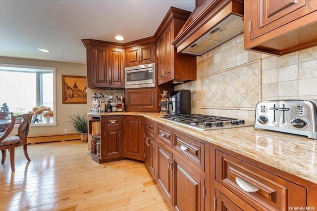 kitchen featuring light stone counters, premium range hood, backsplash, light hardwood / wood-style floors, and appliances with stainless steel finishes