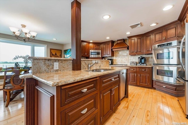 kitchen with sink, stainless steel appliances, premium range hood, a chandelier, and light wood-type flooring