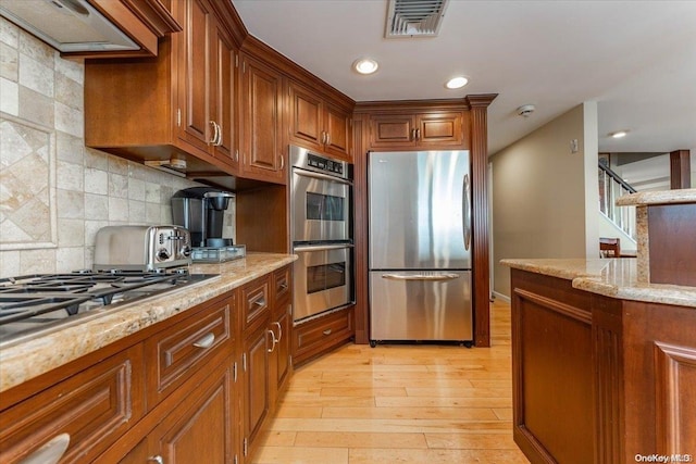 kitchen featuring backsplash, premium range hood, light hardwood / wood-style flooring, light stone counters, and stainless steel appliances