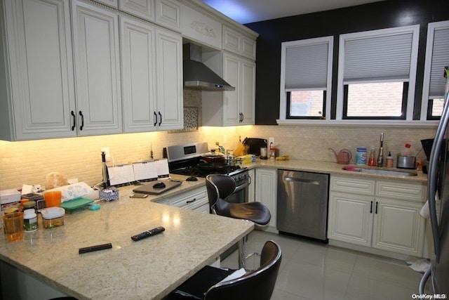 kitchen with wall chimney range hood, sink, light stone countertops, appliances with stainless steel finishes, and tasteful backsplash